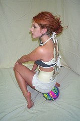 woman facing left from camera, with back facing camera.  She's wearing an back brace, and balancing on a small ball.