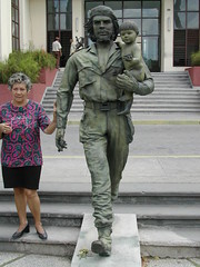 Che Statue outside local communist party HQ in Santa Clara. Woman is explaining the symbolism of the different items found on the statue.<br />
There is a slot on the statue's back. Its real purpose is to prevent the statue from cracking as the material expands and shrinks, but it makes the statue look like a bank. As our professor joked, it was a fitting symbol of the regime’s selling out, or at least capitalizing, on Che’s revolutionary chicness.