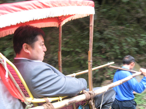 Businessman riding on the shoulders of porters through the park in China