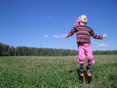 Young girl jumping on top of a grassy hill