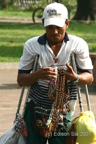 Disabled street vendor on crutches waiting for customer in front Manila Cathedral, religious items, wooden rosaries,  Buhay Pinoy Philippines Filipino Pilipino  people pictures photos life Philippinen Binondo     