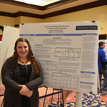 A senior student poses with her poster while presenting it.