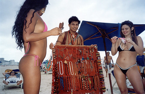 Two girls in string bikini buying bangles from a bangles seller on Ipanema Beach
