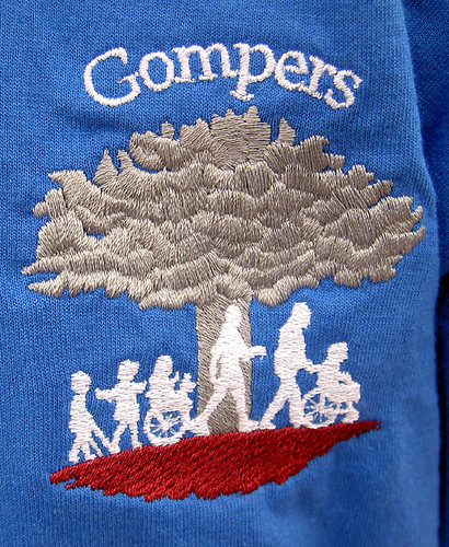 T-shirt with GOMPERS showing a tree and several children and an adult walking.  Some of the children are using crutches or wheelchairs.