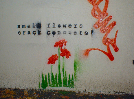 graffiti of green grass with small red flowers poking up and the text, in black, "small flowers / crack concrete"