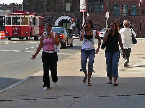 3 women walking together while on cell phones