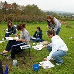 Students sit outside and paint the nature around them.