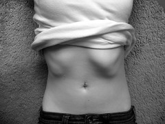 photo is in black and white of a woman's lower torso, with a pronounced rib-cage and a pierced belly button