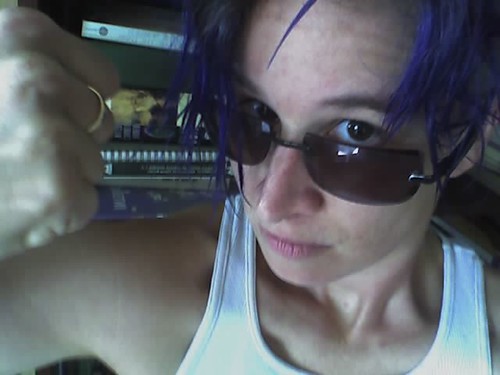 Person with blue hair and sunglasses holding a fist up to the camera.