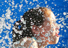 A girl's screwed up face in profile, seen against a blue background, many drops of water splashing out in front of her. Drops by decoder420 on flickr