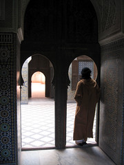 A man wearing a turban and djelaba leaning against and arched doorway and seen in silhouette