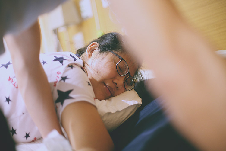 孕婦側著臉靠在枕頭上，丈夫在她身後扶著腰背。