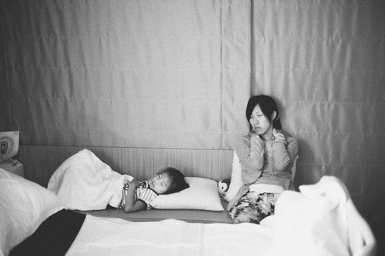 助產師坐在長椅一側，手靠在頸邊，姐姐躺在旁邊睡覺。